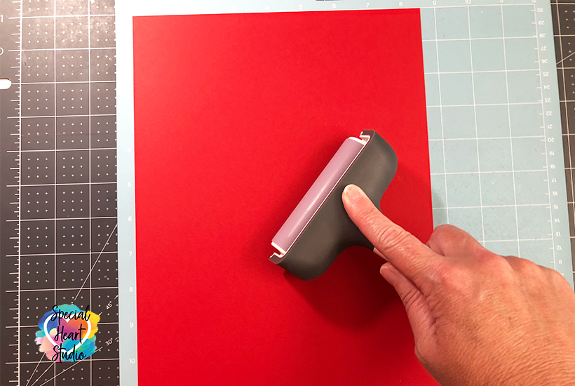 Using a Cricut Brayer to adhere red cardstock to the cutting mat.