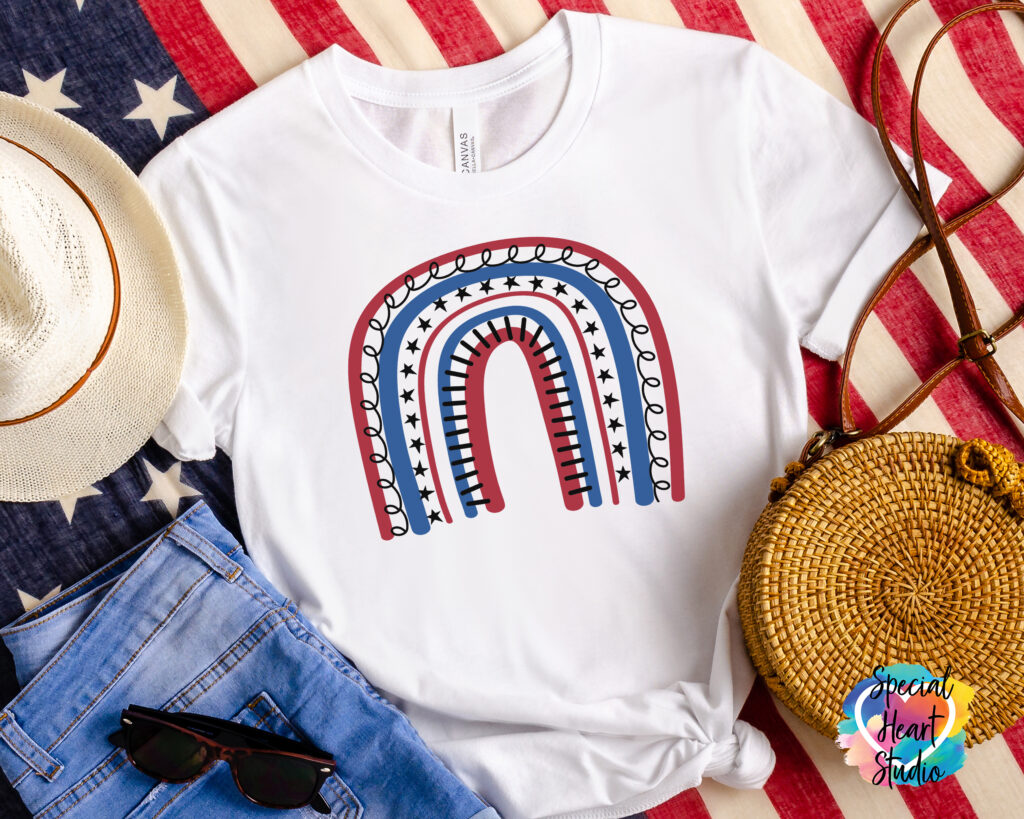 White t-shirt with red, white, and blue rainbow on a flag.  Also in photo jeans, sunglasses a straw hat and purse.