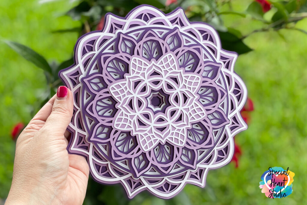 Intricate layered mandala made from purple and white cardstock held outside in front of green grass.